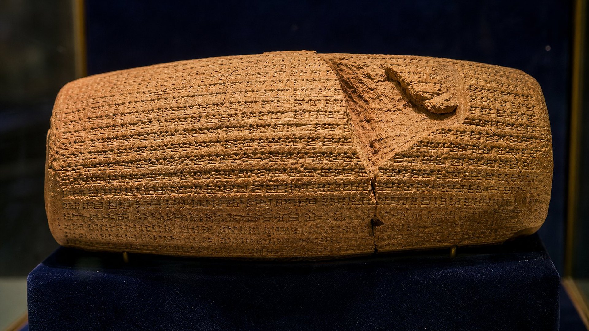 Un cylindre d’argile cuite en forme de tonnelet, couvert de fines lignes d’écriture cunéiforme, posé dans une vitrine sous une lumière rasante.